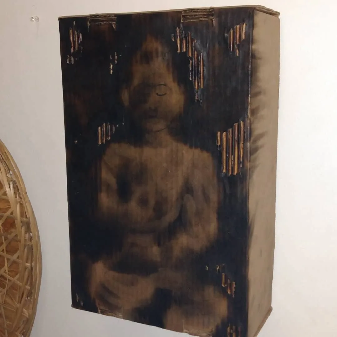 Scorched meditating figure burned into tall cardboard