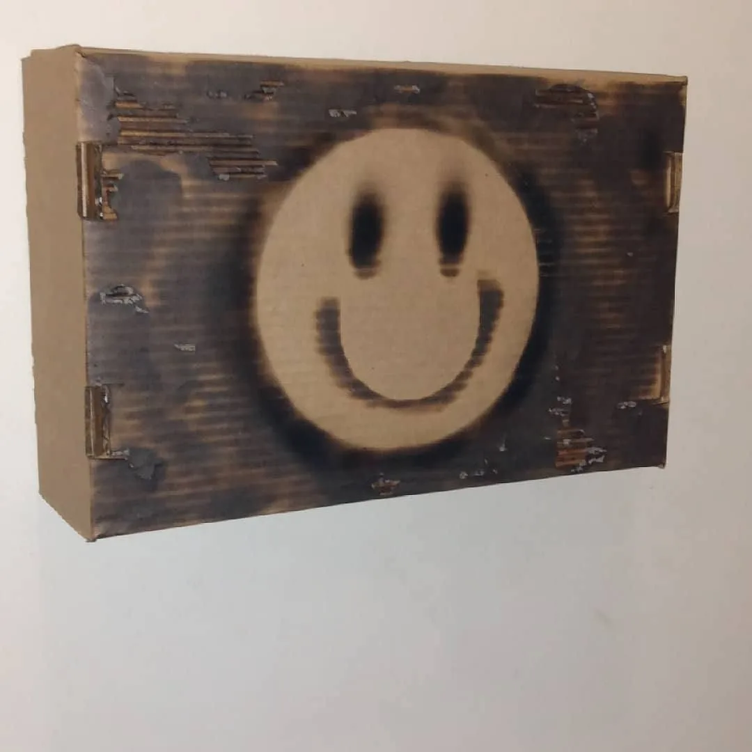 Scorched smiley face burned into a cardboard box
