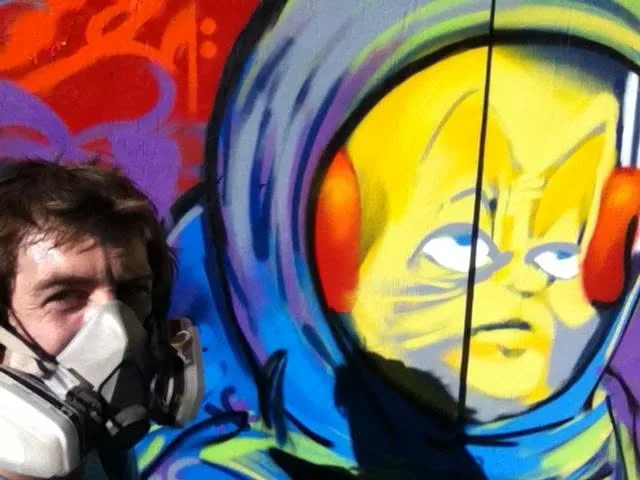 Derek Boe wearing a respirator beside the FUSE mural